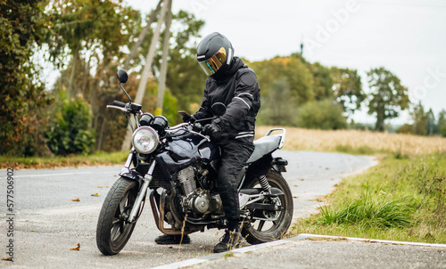 motorcyclist in a helmet and motorcycle clothing stands at an old cafe racer with a smartphone © velimir