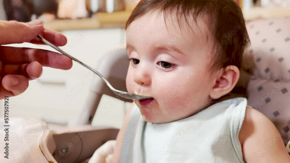 mom feeds baby at the table. dirty a baby newborn dirty mouth eats from a spoon. happy family kindergarten proper nutrition newborn. baby eats fruit puree from a lifestyle spoon mom feeds baby at the table. dirty a baby newborn dirty mouth eats from a spoon. happy family kindergarten proper nutrition newborn. baby eats fruit puree from a lifestyle spoon