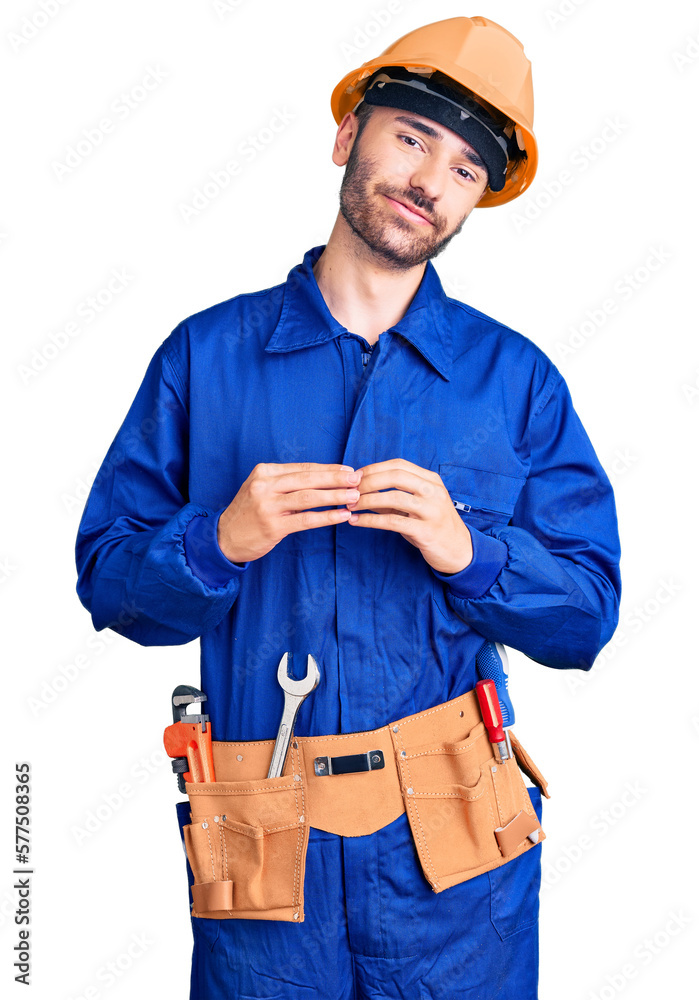 Young hispanic man wearing worker uniform hands together and fingers crossed smiling relaxed and cheerful. success and optimistic