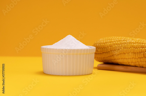 Erythritol, organic sweetener produced by fermentation from corn, called dextrose in ceramic bowl on yellow orange background, bunch of corn. Sugar substitute. Horizontal plane, copy space for text