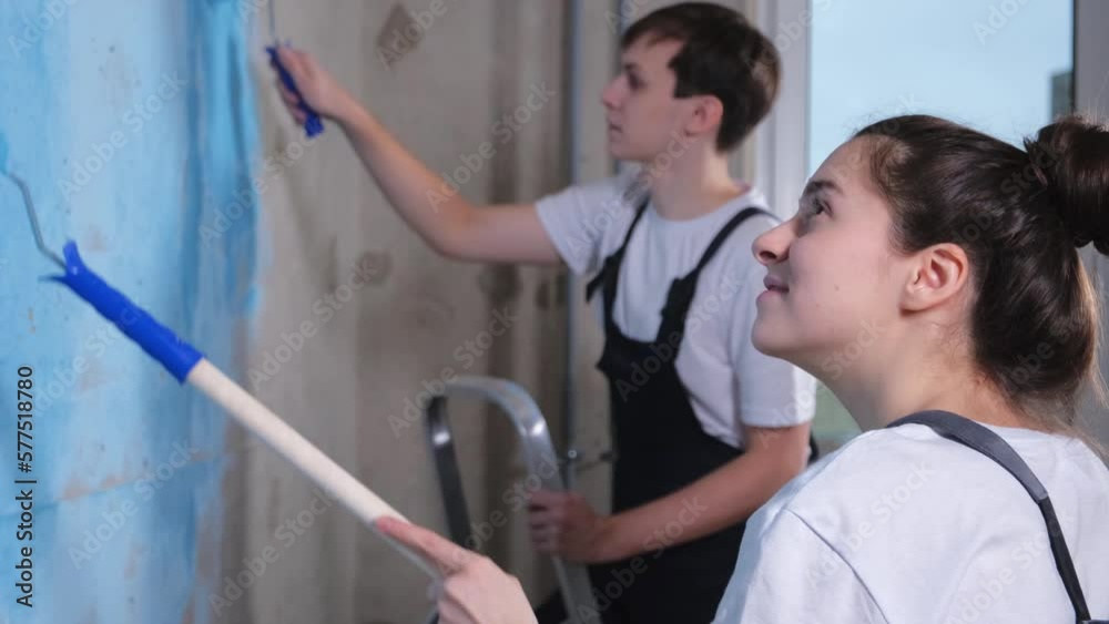 Couple in new home during repair works painting wall together. Happy family holding paint roller