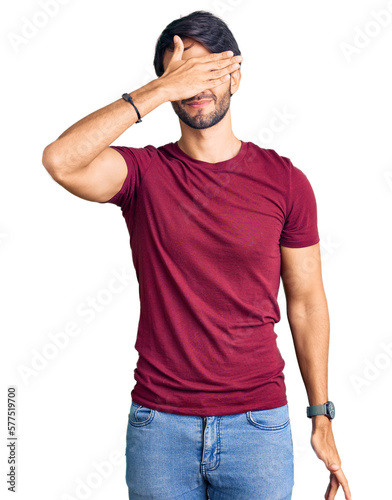 Handsome hispanic man wearing casual clothes covering eyes with hand, looking serious and sad. sightless, hiding and rejection concept