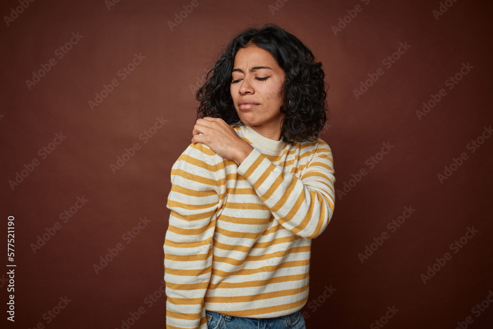 Young colombian curly hair woman isolated on brown background having a shoulder pain. Young colombian curly hair woman isolated on brown background having a shoulder pain.