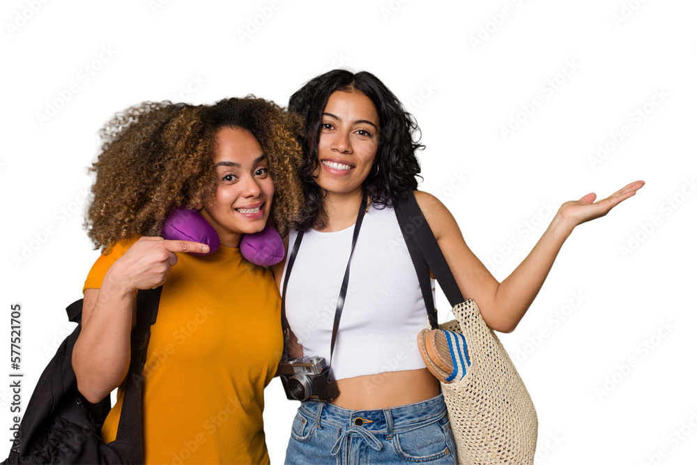 Two diverse friends on a beach vacation with vintage camera, beach bag, and travel pillow showing a copy space on a palm and holding another hand on waist.