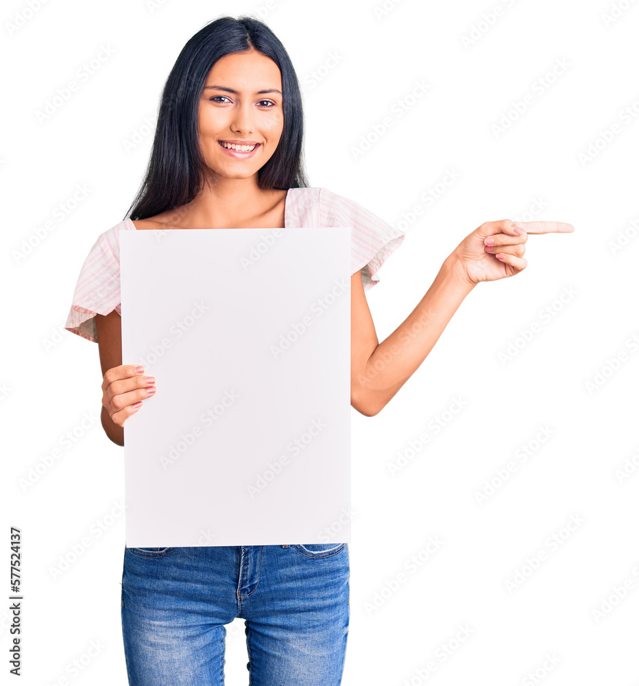 Young beautiful latin girl holding blank empty banner smiling happy pointing with hand and finger to the side Young beautiful latin girl holding blank empty banner smiling happy pointing with hand and finger to the side
