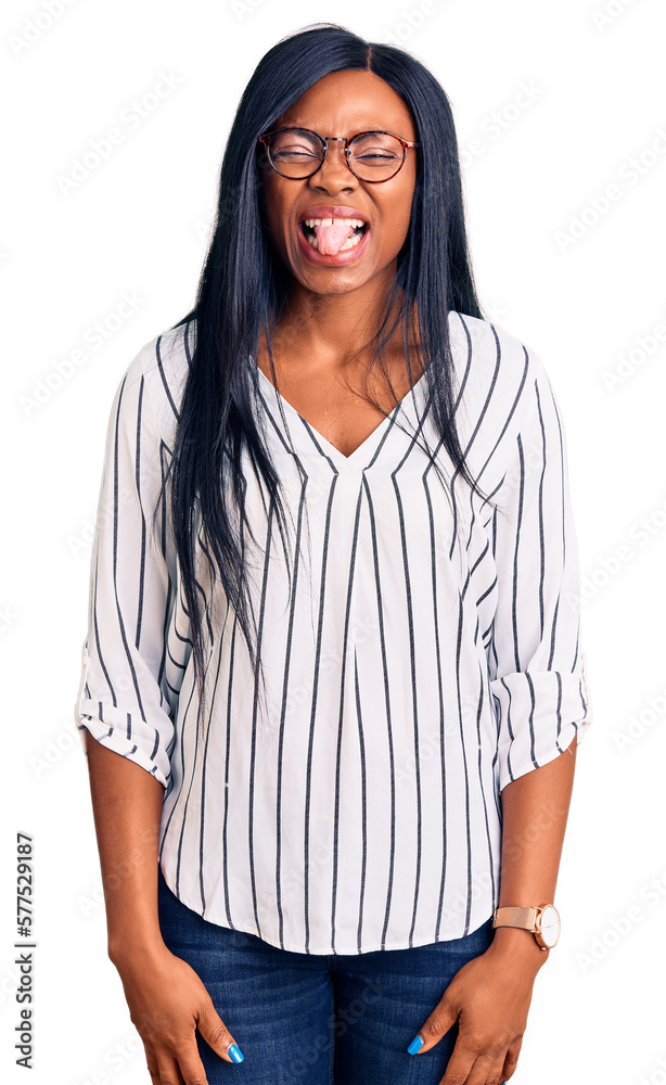 Young african american woman wearing casual clothes and glasses sticking tongue out happy with funny expression. emotion concept. Young african american woman wearing casual clothes and glasses sticking tongue out happy with funny expression. emotion concept.