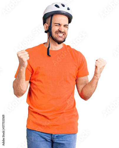 Young handsome man wearing bike helmet very happy and excited doing winner gesture with arms raised, smiling and screaming for success. celebration concept.
