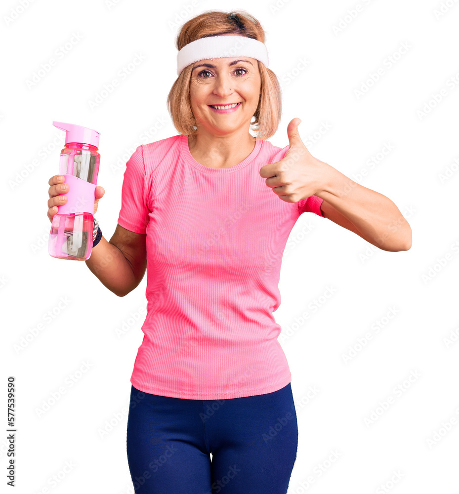 Young blonde woman wearing sportswear holding water bottle smiling happy and positive, thumb up doing excellent and approval sign Young blonde woman wearing sportswear holding water bottle smiling happy and positive, thumb up doing excellent and approval sign