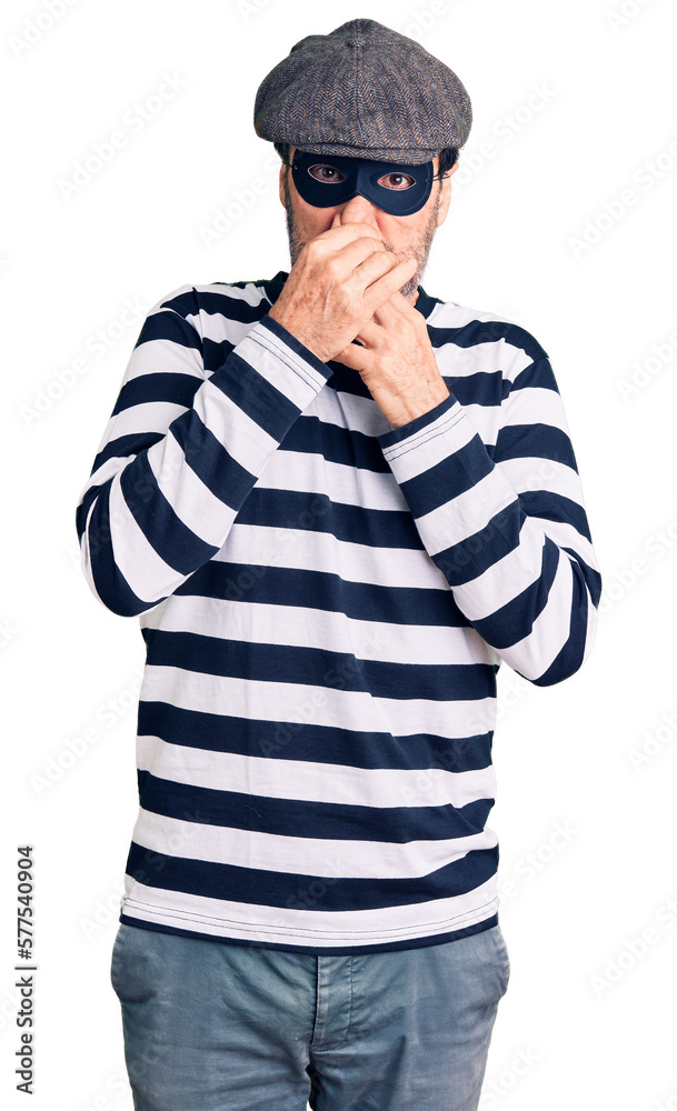 Middle age handsome man wearing burglar mask smelling something stinky and disgusting, intolerable smell, holding breath with fingers on nose. bad smell Middle age handsome man wearing burglar mask smelling something stinky and disgusting, intolerable smell, holding breath with fingers on nose. bad smell