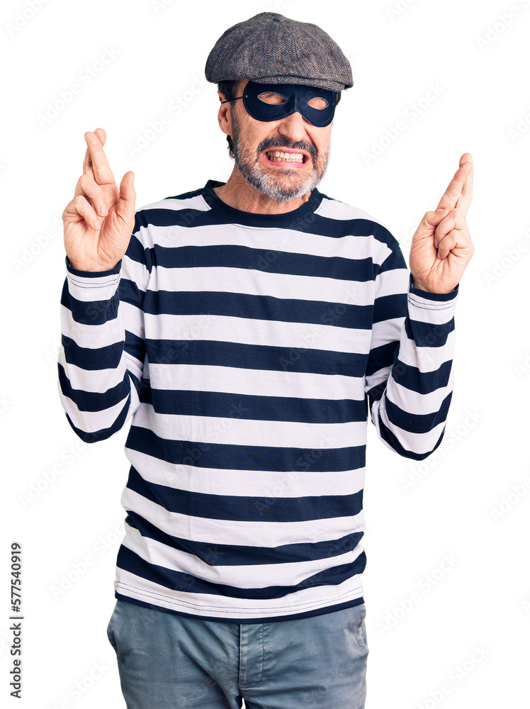 Naklejka premium Middle age handsome man wearing burglar mask gesturing finger crossed smiling with hope and eyes closed. luck and superstitious concept.