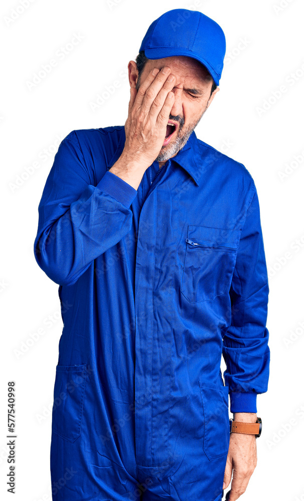 Middle age handsome man wearing mechanic uniform yawning tired covering half face, eye and mouth with hand. face hurts in pain.