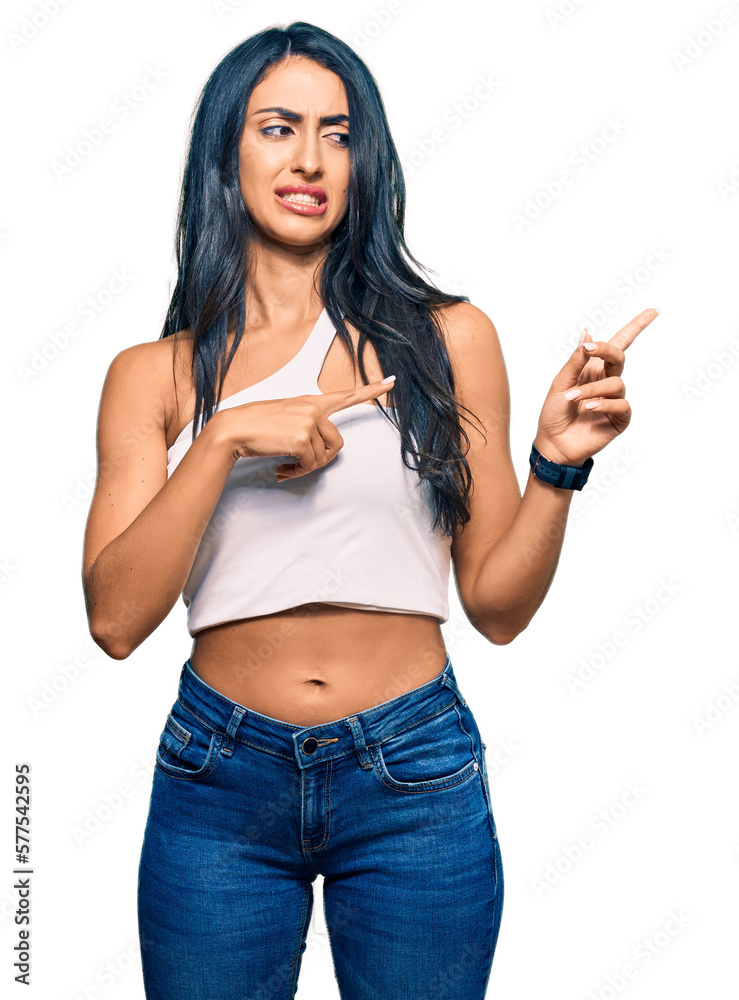 Beautiful hispanic woman wearing casual clothes pointing aside worried and nervous with both hands, concerned and surprised expression Beautiful hispanic woman wearing casual clothes pointing aside worried and nervous with both hands, concerned and surprised expression