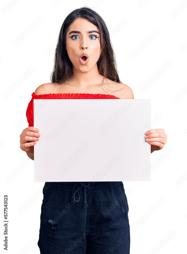 Brunette teenager girl holding blank empty banner scared and amazed with open mouth for surprise, disbelief face Brunette teenager girl holding blank empty banner scared and amazed with open mouth for surprise, disbelief face