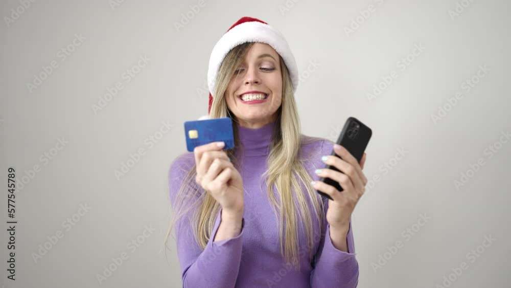 Young blonde woman wearing christmas hat using smartphone and credit card over isolated white background Young blonde woman wearing christmas hat using smartphone and credit card over isolated white background