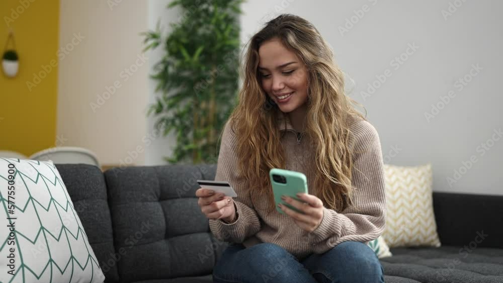 Young beautiful hispanic woman using smartphone and credit card sitting on sofa at home Young beautiful hispanic woman using smartphone and credit card sitting on sofa at home