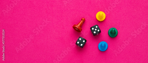 Colorful game chips and two dice are placed on an rhodamine red background