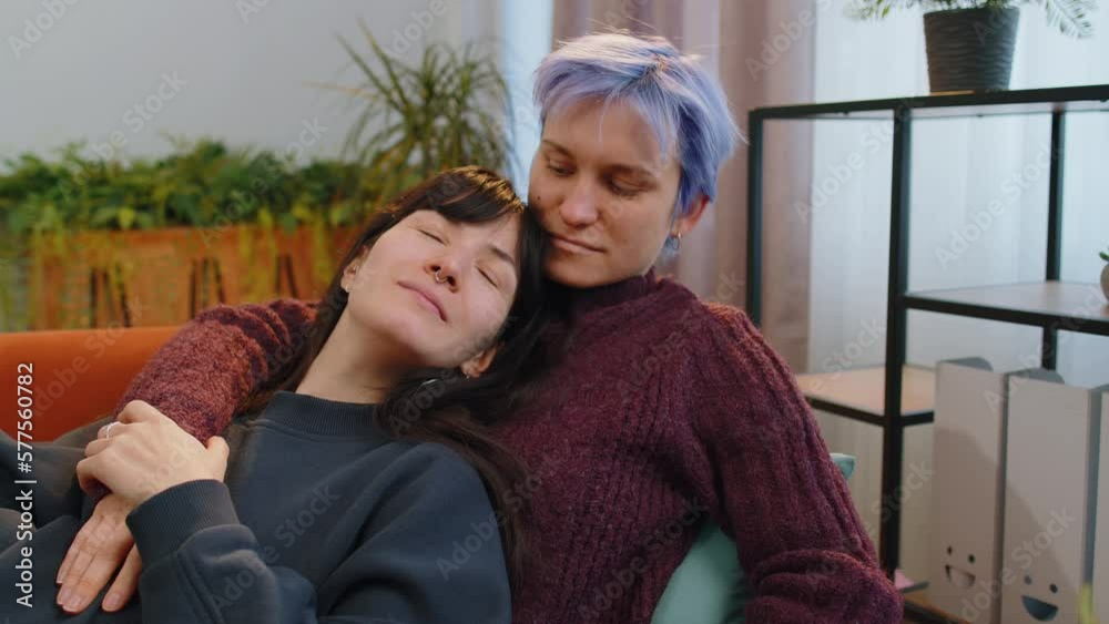 Two young lesbian women family couple at modern home living room. Loving same sex female gay girls hugging, relaxing together, lie on sofa. LGBT people. Romantic love relationship concept and emotion Two young lesbian women family couple at modern home living room. Loving same sex female gay girls hugging, relaxing together, lie on sofa. LGBT people. Romantic love relationship concept and emotion