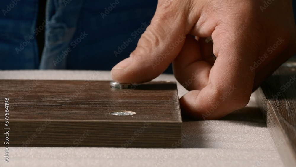 Close-up of man inserting screws into wooden board. Creative. Carpenter screws screws into holes of wooden board. Screwing screws into wooden board