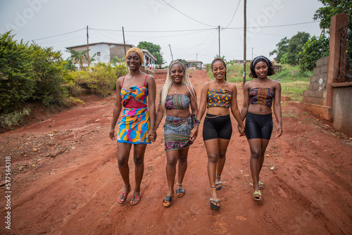 Four young smiling African women walk holding hands, women dressed with traditional African clothes photo