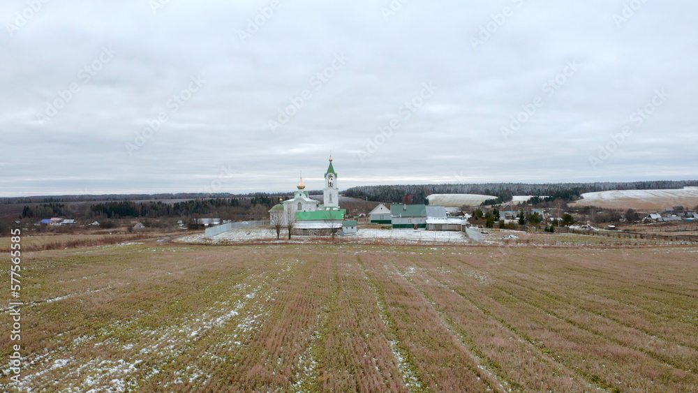 Initial winter. Clip.View from a drone on a landscape with snowy grass in a field where there is a temple with a golden cross on a golden dome against the blue sky.