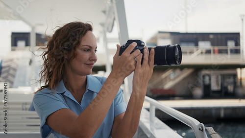 Beautiful woman taking pictures on the ship. Action. A young photographer with curly hair blowing on sees and sits and takes a photo of a wonderful summer seascape.