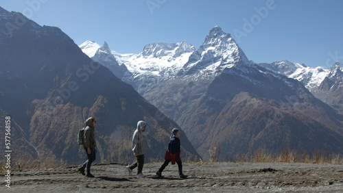 Family walks on background of mountain valley with snowy peaks. Creative. Women with child are walking in mountain valley on sunny day. Family hiking with child in valley with rocky mountains