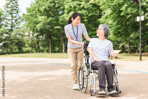 公園を散歩する車椅子の高齢者と介護士・看護師・理学療法士・運動指導員の女性 