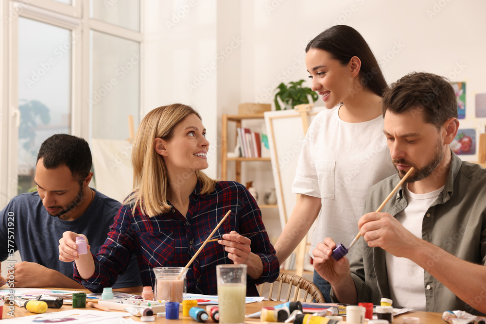 Fototapeta premium Artist teaching her students to paint at table in studio. Creative hobby