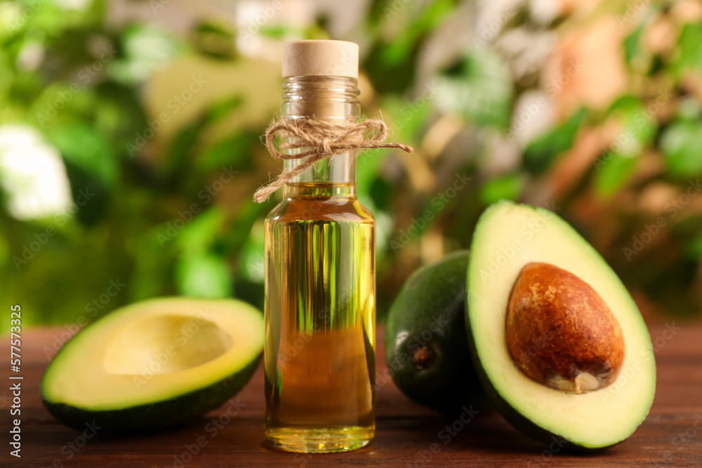 Glass bottle of cooking oil and fresh avocados on wooden table against blurred green background Glass bottle of cooking oil and fresh avocados on wooden table against blurred green background