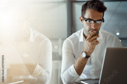 Mmm...I wonder. Cropped shot of a handsome young businessman looking thoughtful while working on his laptop in the office.