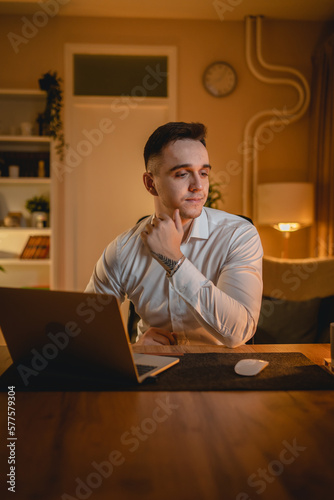 A young man is working late or studying at his home office while drinking coffee and using his mobile phone