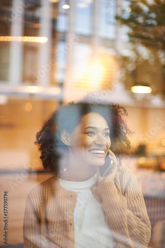 View through the window to a cheerful African American woman smiling while talking on mobile phone