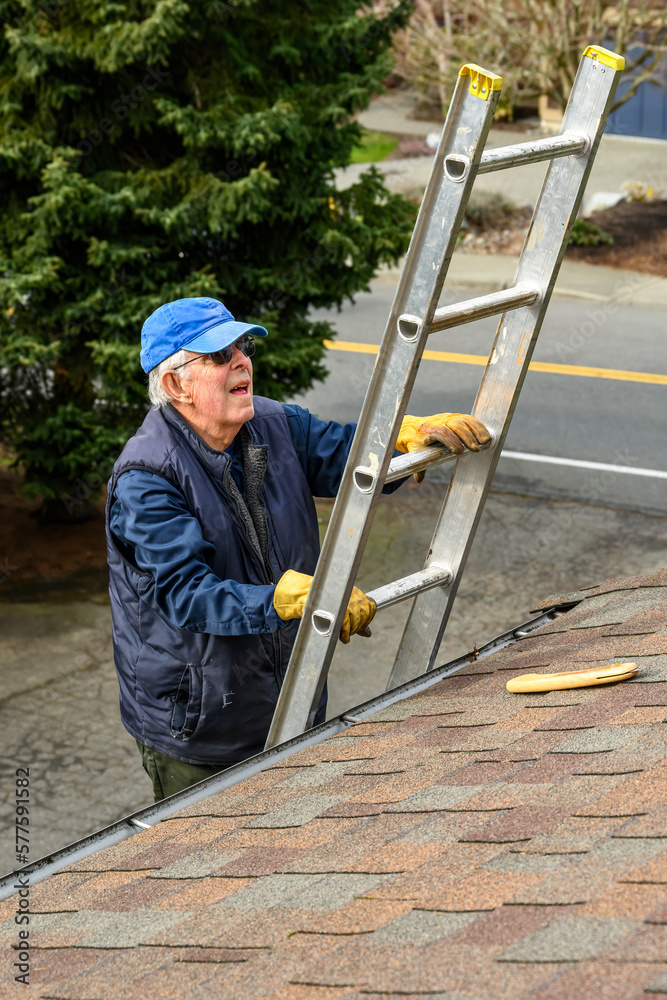 Senior man wearing leather work gloves climbing an aluminum extension ladder up to a rooftop 