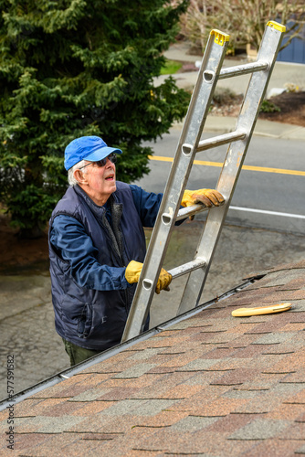 Senior man wearing leather work gloves climbing an aluminum extension ladder up to a rooftop 