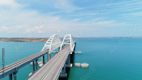 A long bridge for vehicles to cross the ocean. Drone view. Shot. A beautiful panorama overlooking the sunny clear sky and cars moving over a huge clear pond.