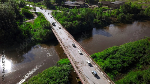 Aerial view of a river and a bridge with driving cars on a summer day. Clip. Summer village surrounded by green vegetation.