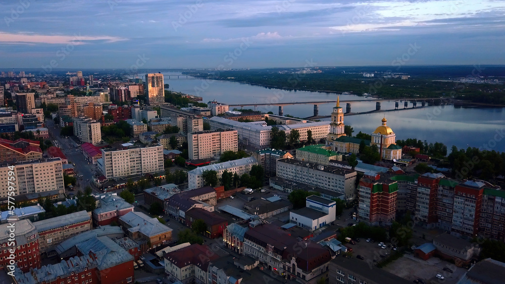 Aerial view of the sunset sky above the wide river. Clip. Green town located along the river.