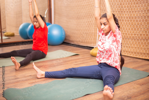 Young indian teenager girls practicing stretching yoga asana exercise at indoor studio, full length.
