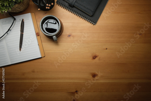 Above view of wooden working desk with cup of coffee, notebook, glasses and alarm clock. Copy space for text.