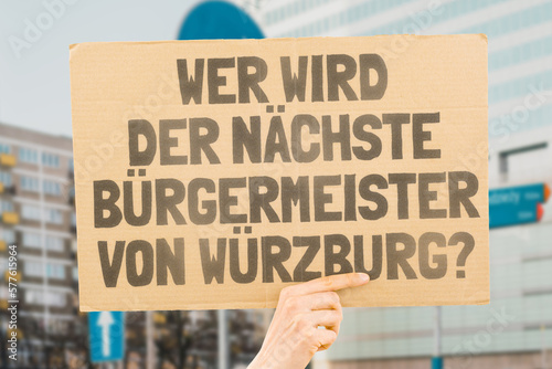 The question " Who's the next mayor of Würzburg? " on a banner in men's hands blurred the background. Election. City management. Politics. Urban. Voter. Candidate