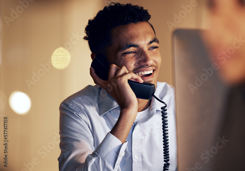 Telephone, night and businessman on a phone call in the office talking while working on a computer. Discussion, communication and professional male employee speaking on a landline in the workplace.