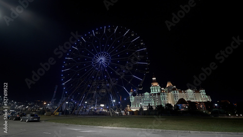 Low angle view of the ferris wheel in front of a castle. Action. Summer evening out of town, concept of tourism.