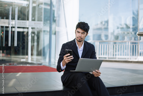 Entrepreneur working on laptop, tablet while sitting at the urban street. Handsome businessman carrying laptop bag and doing business outside in the city street.