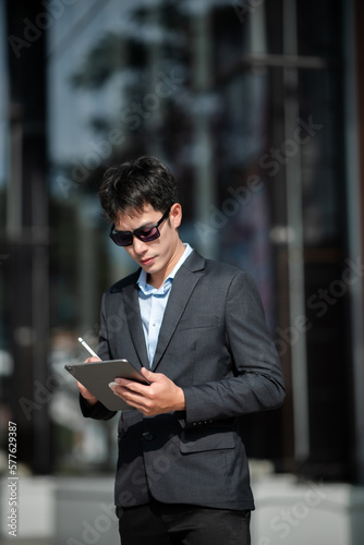 Asian businessman using a tablet and laptop on a bench in the city