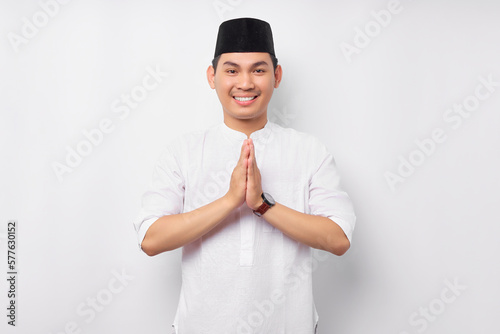 Happy smiling young Asian Muslim man in Arabic costume standing with gesturing Eid Mubarak greeting and welcoming Ramadan isolated on white background. People religious Islamic lifestyle concept