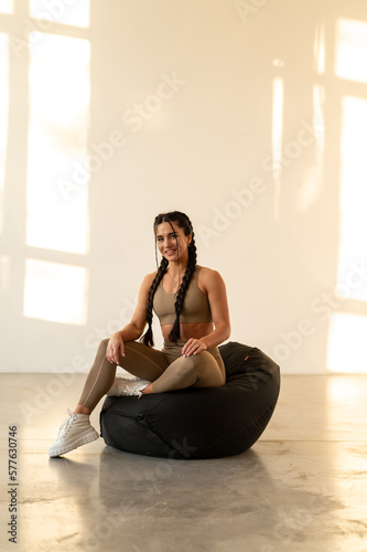 Athletic attractive girl in fitness clothes posing sitting on a pouf. Rest after training. Black and white photo