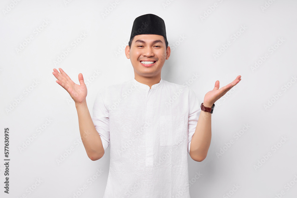 Smiling friendly handsome young Asian Muslim man wearing Arabic costume standing with wide raised arms and welcoming Ramadan isolated over white background. People religious Islamic lifestyle concept