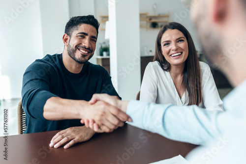 Murais de parede Attractive real-estate agent shaking hands with young couple after signing agreement contract in the office