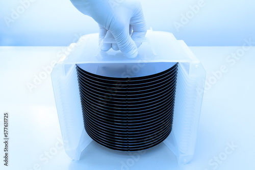 Silicon wafer inspection. A batch of silicon wafers packed in a plastic storage box in the clean room of a semiconductor foundry ready for microchip production.