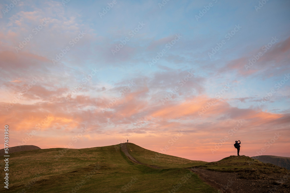 Beautiful colorful Winter sunset landscape over Latrigg Fell in Lake District with two people on hilltop admiring sunset